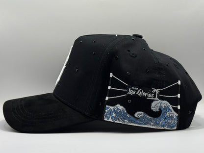 Black cap with wave design and 'Las Glorias' branding on a white surface